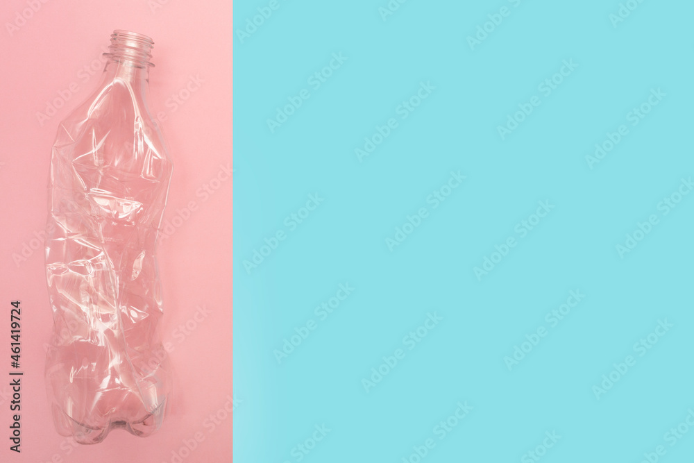 Used and crumpled plastic bottle on pink and blue background with a place for text. Recycling concept. Rumpled. Reasonable consumption. Flat lay. Copy space. Used and crumpled plastic bottle on pink and blue background with a place for text. Recycling concept. Rumpled. Reasonable consumption. Flat lay. Copy space.