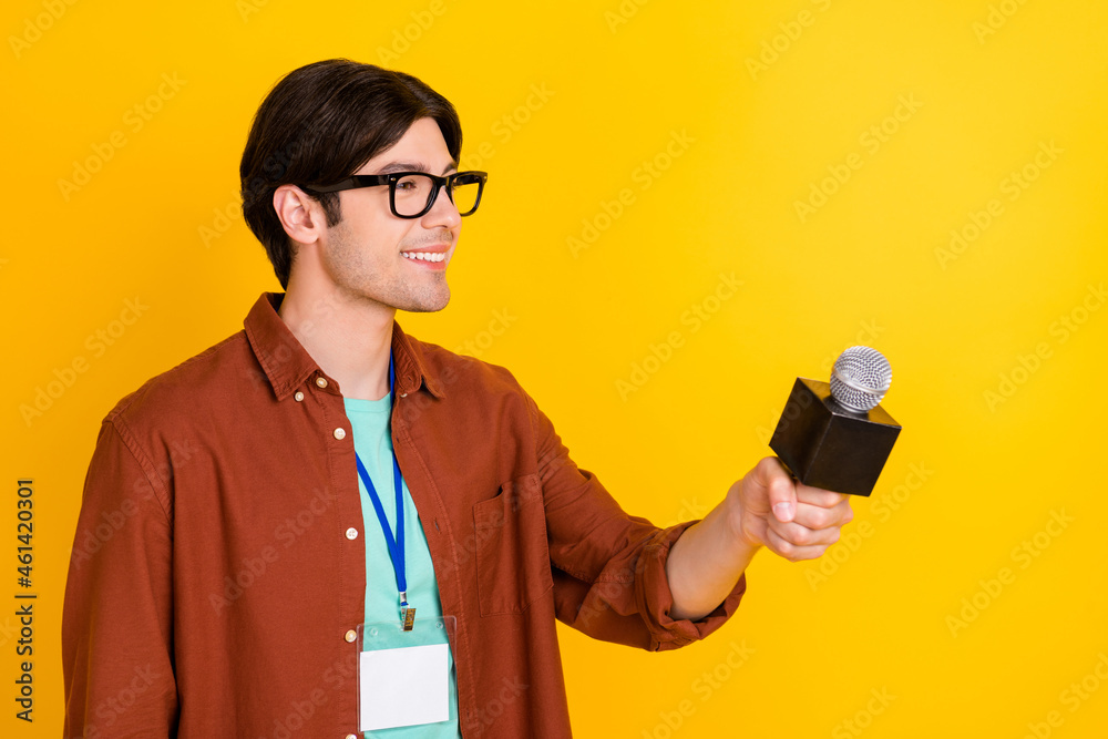 Photo of funny cute young man wear brown shirt smiling holding mic looking empty space isolated yellow color background Photo of funny cute young man wear brown shirt smiling holding mic looking empty space isolated yellow color background