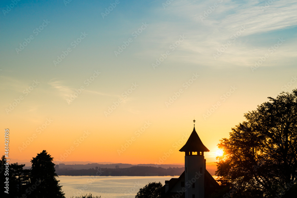 Fototapeta premium Sunset over Lake Zugersee from the Swiss town of Zug, silhouetted by a church tower.