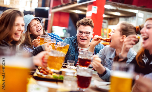Happy friends drinking beer with mixed food at indoor venue - Social gathering life style concept on young people enjoying hangout time eating together - Vivid filter with shallow depth of field