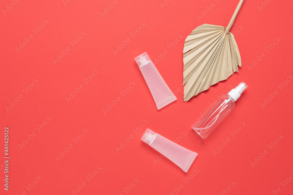 Cosmetic spray transparent bottle, tube with dry palm leaf on on a red paper background. Top view, flat lay, copy space. Travel concept