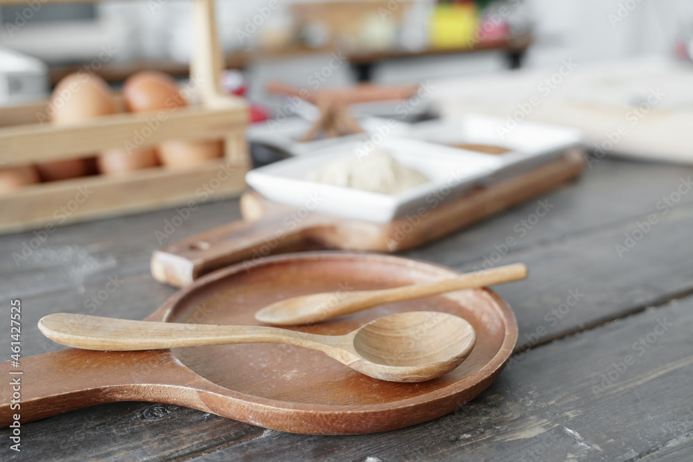 Selective focus on wooden spoon on tray with raw ingredients, flour, cinnamon powder, eggs, kitchen utensils for bakery on wooden table at home kitchen Selective focus on wooden spoon on tray with raw ingredients, flour, cinnamon powder, eggs, kitchen utensils for bakery on wooden table at home kitchen