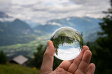 Hand holding glass sphere in front of valley in the alps