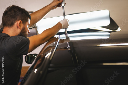 Close shot of a mechanic in protective gloves in process of removing dents from the roof of the car at the service station.