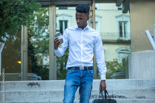 young black man office worker walking down stairs with satisfaction looking at glass of coffee leaving work photo