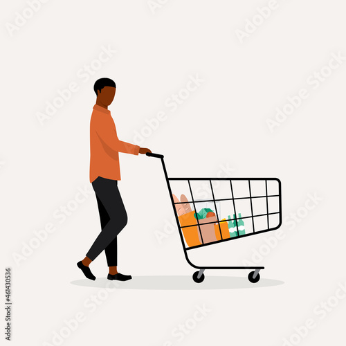 Young Black Man Customer Pushing Shopping Cart With Groceries Inside.