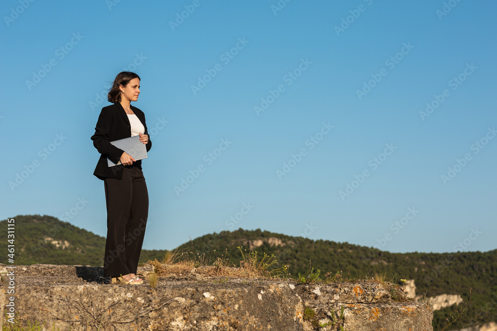 Confident businesswoman with laptop standing on rock top Confident businesswoman with laptop standing on rock top