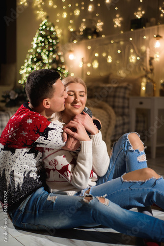 Couple in knit sweaters near Christmas tree. Man and woman in Christmas interior room. © nagaets