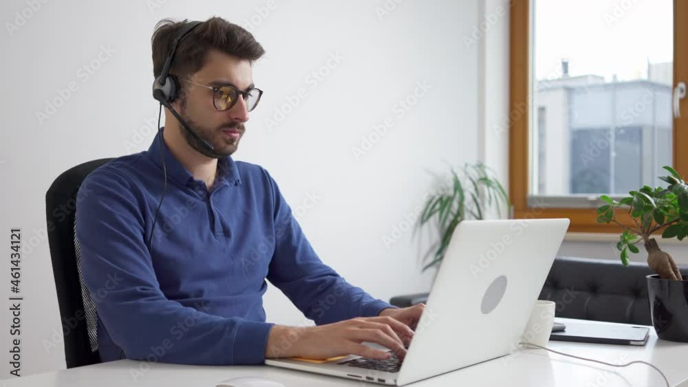 Young man typing on laptop working from home with headset Young man typing on laptop working from home with headset