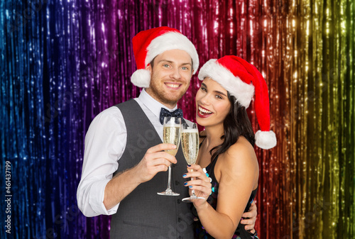 celebration, people and winter holidays concept - happy couple in santa hats with glasses of non alcoholic champagne at christmas party over foil fringe on background