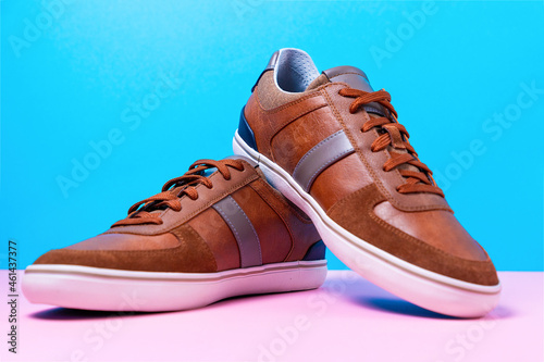 Pair of male's new sneakers made of brown leather laid out on a blue-pink background. Close up © _KUBE_