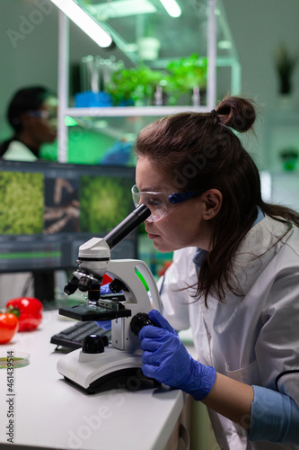 Biologist researcher doctor woman analyzing leaf sample using medical microscope during genetically modified plant experiment. Chemist scientist working in pharmaceutical hospital laboratory