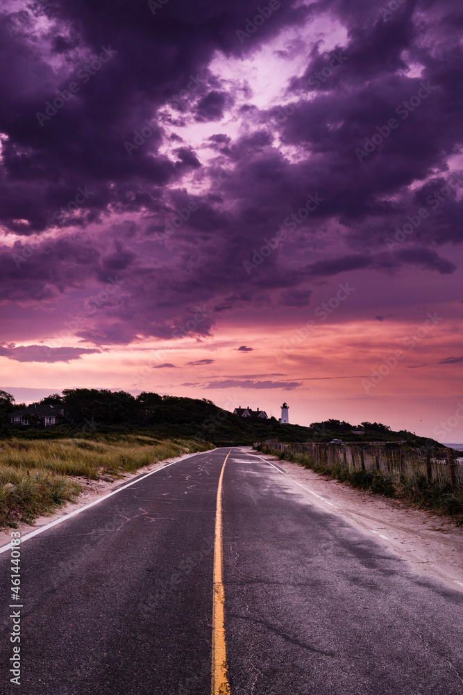 Dramatic purple clouds over the two-lane coastal road heading to the lighthouse. Moody tranquil Cape Cod in autumn.