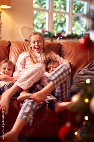 Three Children Wearing Pyjamas Opening Gifts Around Christmas Tree At Home