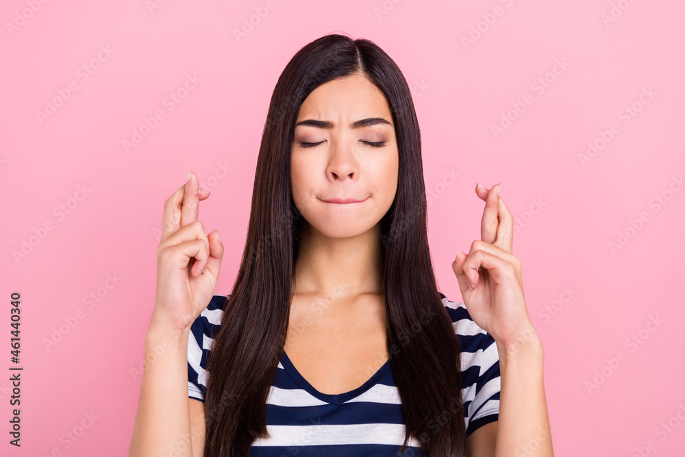 Photo of shiny guilty young woman wear striped outfit closed eyes fingers crossed biting lips isolated pink color background