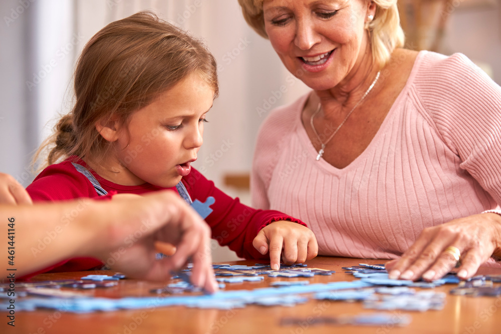 Fototapeta premium Granddaughter With Grandmother Sitting Around Table At Home Doing Jigsaw Puzzle Together