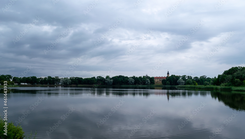 Beautiful clouds are reflected in the lake overlooking the ancient castle of the Radziwills in Nesvizh, Belarus. Summer landscape with architectural elements.