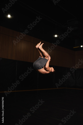 Canvas Print barefoot and shirtless gymnast doing somersault while training in gym