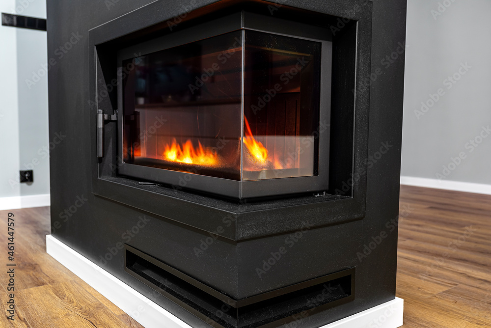 Naklejka premium Burning wood in a modern fireplace with a closed combustion chamber standing in the living room, painted black, with a corner pane.