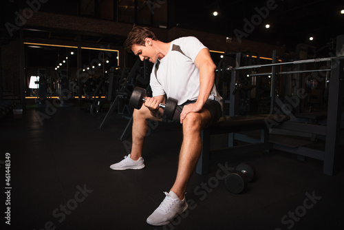 full length view of athletic man in sportswear training with dumbbell in gym.