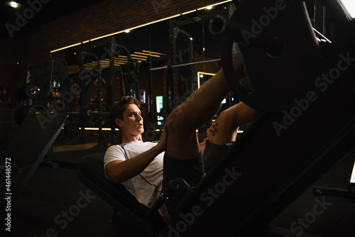 athletic man working out on leg extension exercising machine in sports center.