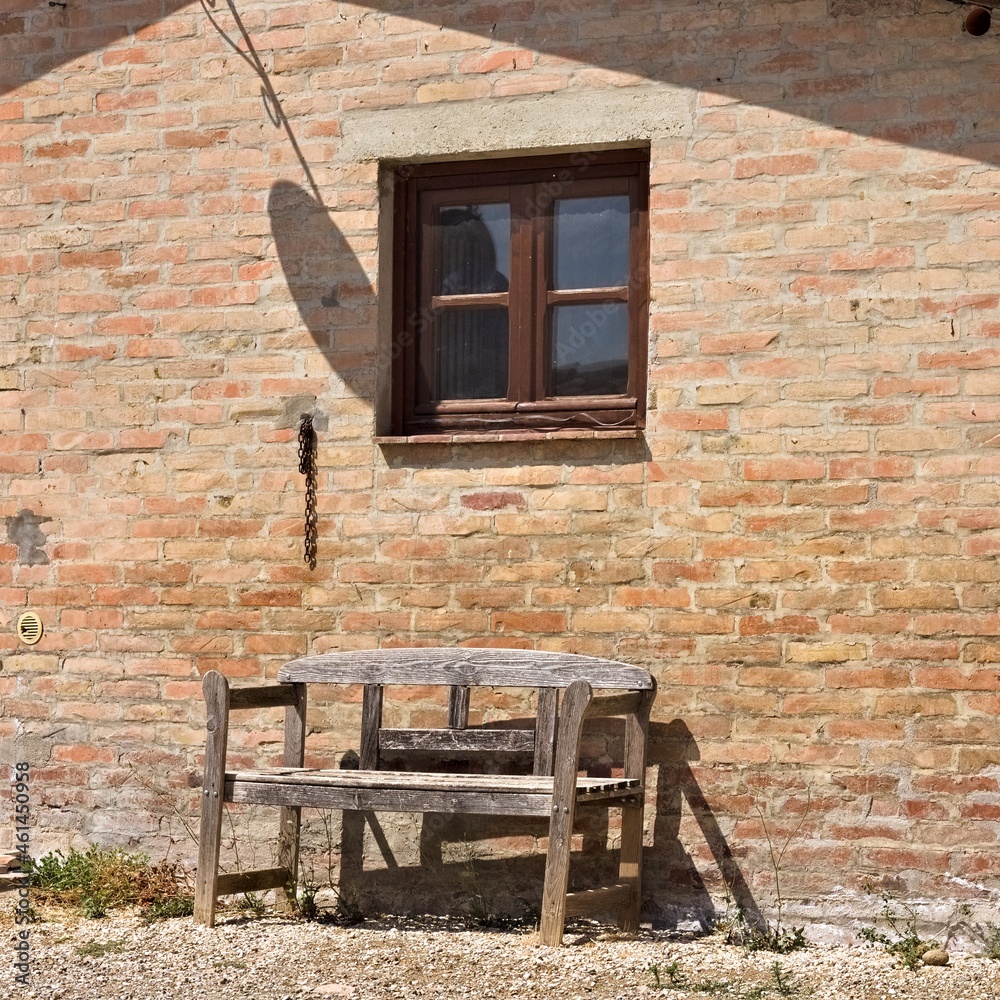 An old wooden bench under a wooden window of a stone farmhouse in the italian countryside (Tuscany, Italy, Europe)