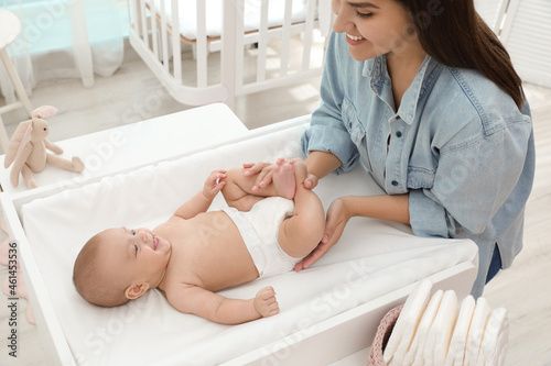 Tablou pe pânză Mother changing her baby's diaper on table at home