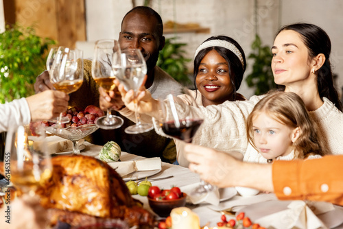 Happy family celebrate Thanksgiving day, sitting at table with roasted turkey and holiday traditional food, dishes. Drinking wine