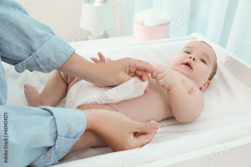 Mother changing baby's diaper at home, focus on hands