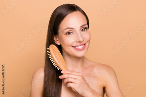 Portrait of attractive cheerful straight-haired woman combing smoothing hair everyday isolated over beige pastel color background