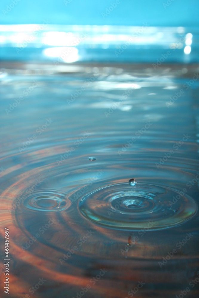 Gotas cristalinas en el aire rebotando  sobre superficie lìquida formando hermosa ilustraciòn con ondas en cìrculo sobre el agua con fondo azul en la bandeja de vidrio.