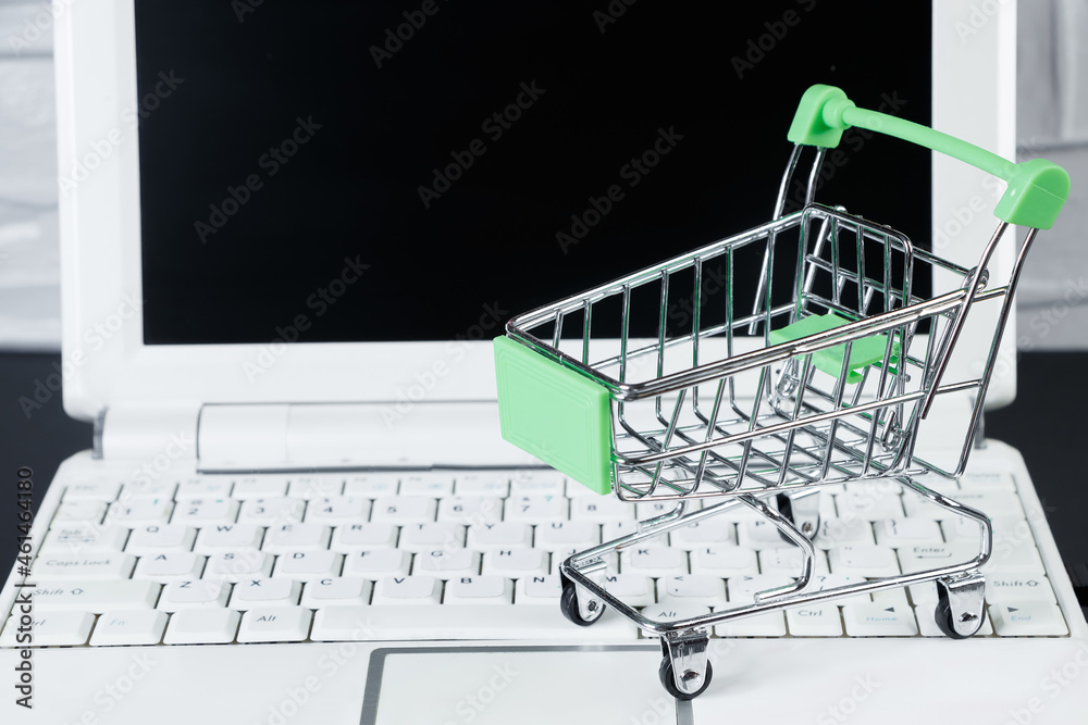 Online sale and Black Friday concept. Laptop and mini shopping cart on white background.