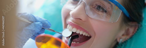 Dentist treating teeth to woman patient using curing light and dental instruments