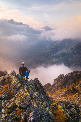 Male hiker takes a break and enjoys mountain views. Female hiker backpacker sitting on the peak edge and enjoying mountains view valley during heavy mist