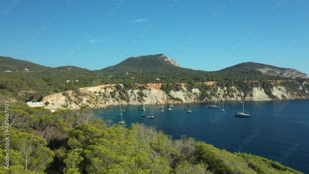 Cliffs that surround the beach of Cala dHort. Many boats and sailboats anchored in front of the beach, seen from the air by a drone. Cliffs that surround the beach of Cala dHort. Many boats and sailboats anchored in front of the beach, seen from the air by a drone.
