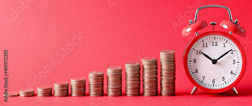 Billede på lærred Ascending stacks of coins aligned with red alarm clock for ten in morning on red