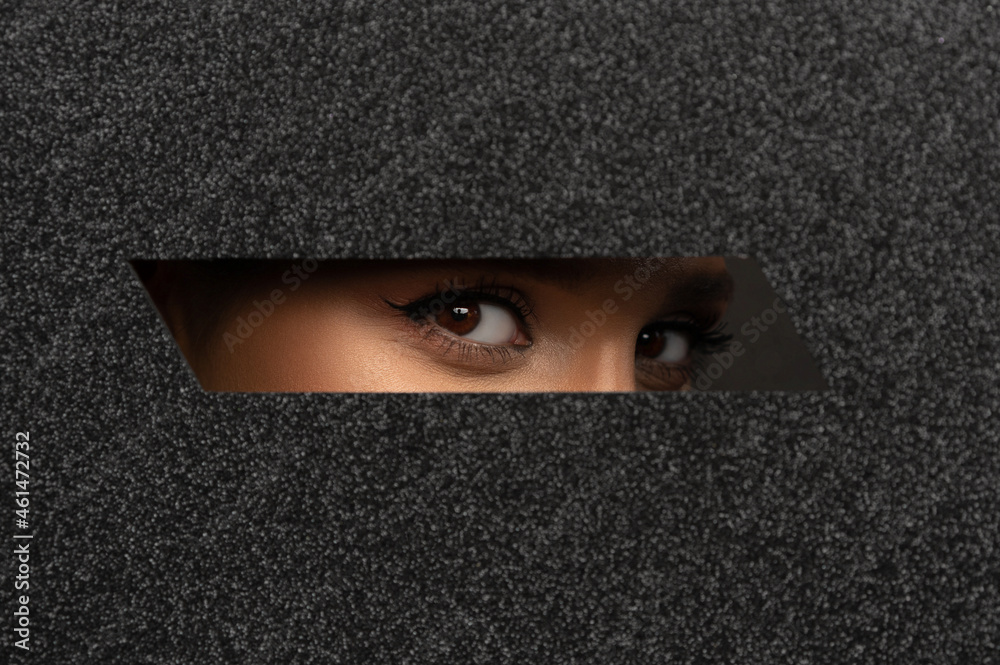 Woman with beautiful brown eyes with brown shadows and expressive eyebrows looks into the hole of shiny black paper