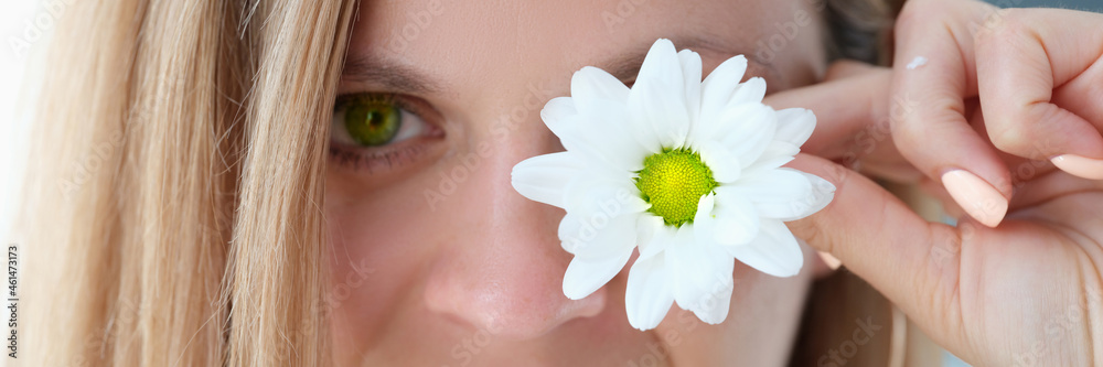 Portrait of beautiful young woman with green eyes closes one eye with flower Portrait of beautiful young woman with green eyes closes one eye with flower