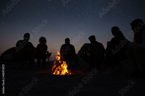 Group of friends gathering around bonfire in evening. Camping season