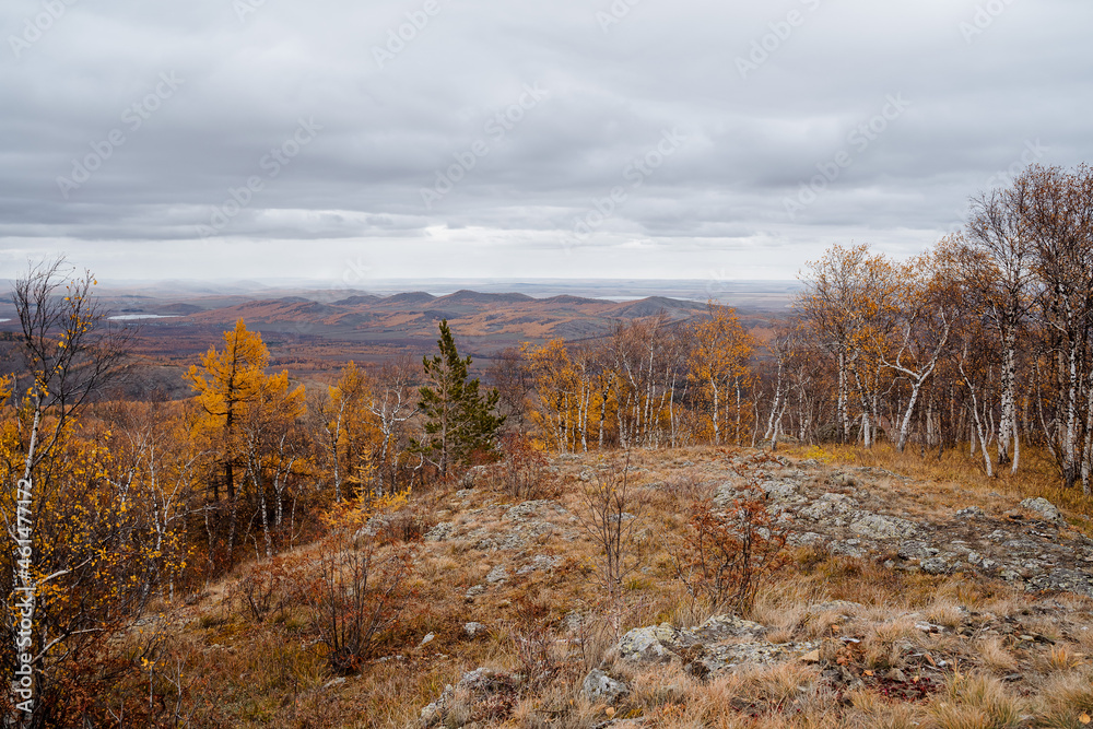 Mountain landscape in cloudy weather, mountains covered with autumn forest, obese clouds fly low over the horizon.