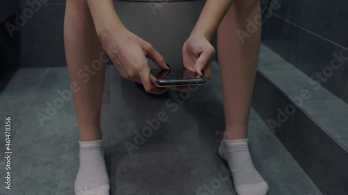 Young woman sitting on a toilet using her mobile phone