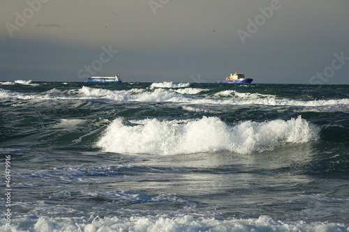 Rough waters at Skagen Nordstrand with two cargo ships in the background near Cape Grenen, meeting point of Skagerrak and Kattegat and the northernmost point of Denmark, Skagen, Northern Jutland, Denm