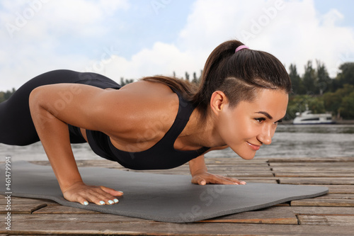 Young woman doing plank exercise on wooden pier near river