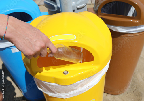 Fotografie used glass bottle into the yellow bin for separate waste collection on the beach
