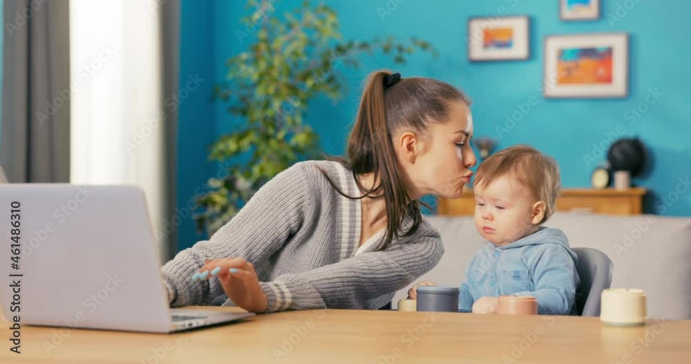 Hard-working, ambitious girl fills out paperwork on computer at table in living room, boy sits next to her looking at laptop, woman kisses her son tenderly on head and goes back to her duties Hard-working, ambitious girl fills out paperwork on computer at table in living room, boy sits next to her looking at laptop, woman kisses her son tenderly on head and goes back to her duties