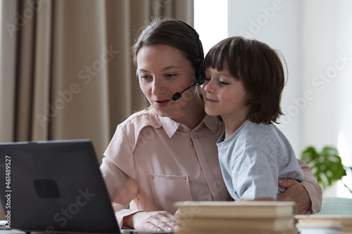 Принти на полотні Young female tutor working and learning remotely from home on video conference when son rushes up and distracts and upsets mother