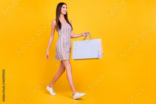 Full length body size woman smiling happy walking with packages looking copyspace isolated vivid yellow color background