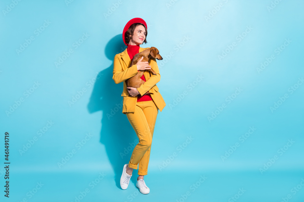 Photo of sweet adorable young woman dressed red headwear holding dog looking empty space smiling isolated blue color background Photo of sweet adorable young woman dressed red headwear holding dog looking empty space smiling isolated blue color background