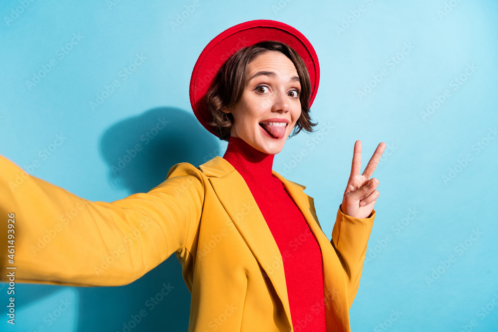 Photo of young girl happy positive smile make selfie grimace tongue-out show peace v-sign isolated over blue color background Photo of young girl happy positive smile make selfie grimace tongue-out show peace v-sign isolated over blue color background