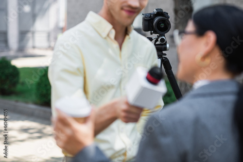 modern digital camera on tripod near blurred reporter taking interview with businesswoman